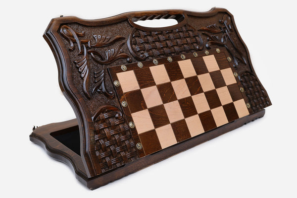 Large carved folding chess board standing open, showing the chessboard, basket-weave and foliate carving and carry-handle cutout