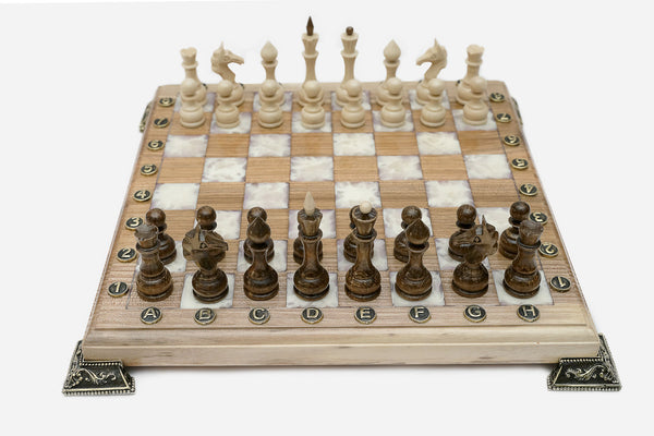 Chess board in pale wood with white marbled epoxy squares, brass corner brackets and wooden pieces set up for play