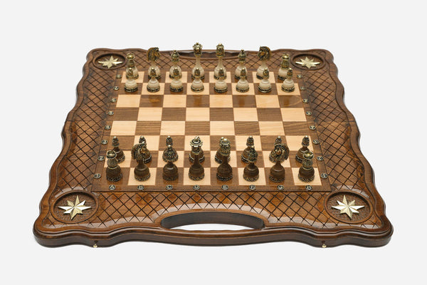 Carved chess board with four brass star inlays, lattice borders and ornate bronze-and-cream figural pieces set up for play