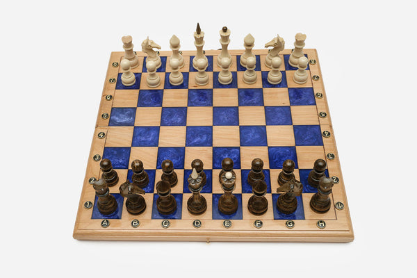 Compact folding chess board in pale wood with royal-blue epoxy squares and wooden pieces set up for play