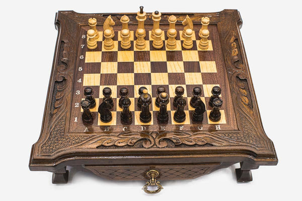 Compact dark walnut chess set with scroll-carved corners and Staunton pieces set up on the inlaid board