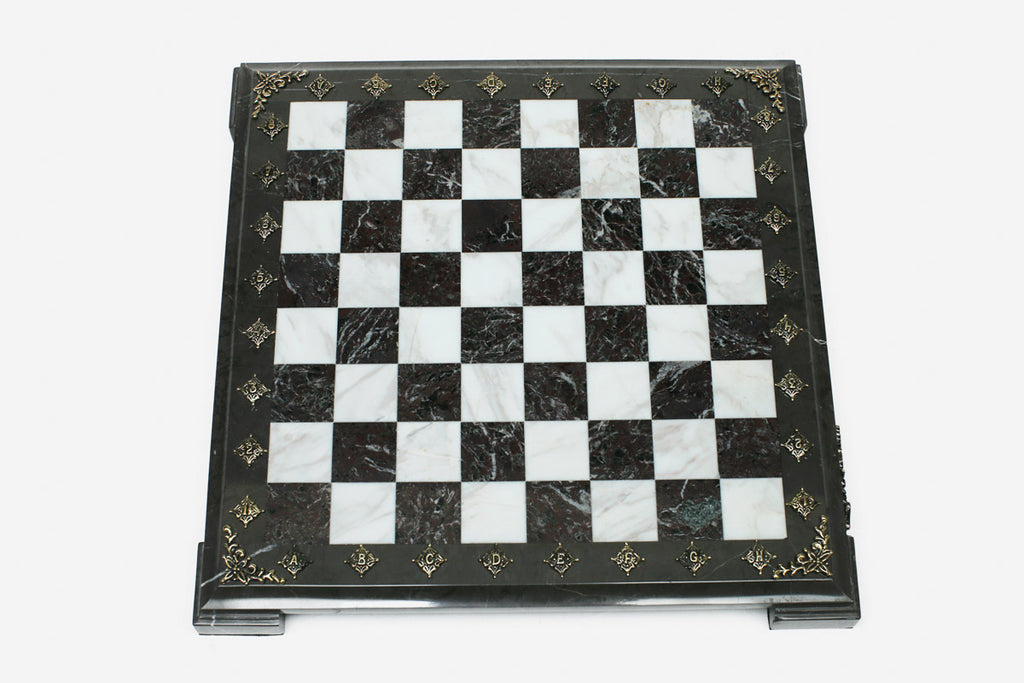 Top-down view of the empty burgundy and white marble chess board with a grey border and brass coordinate medallions