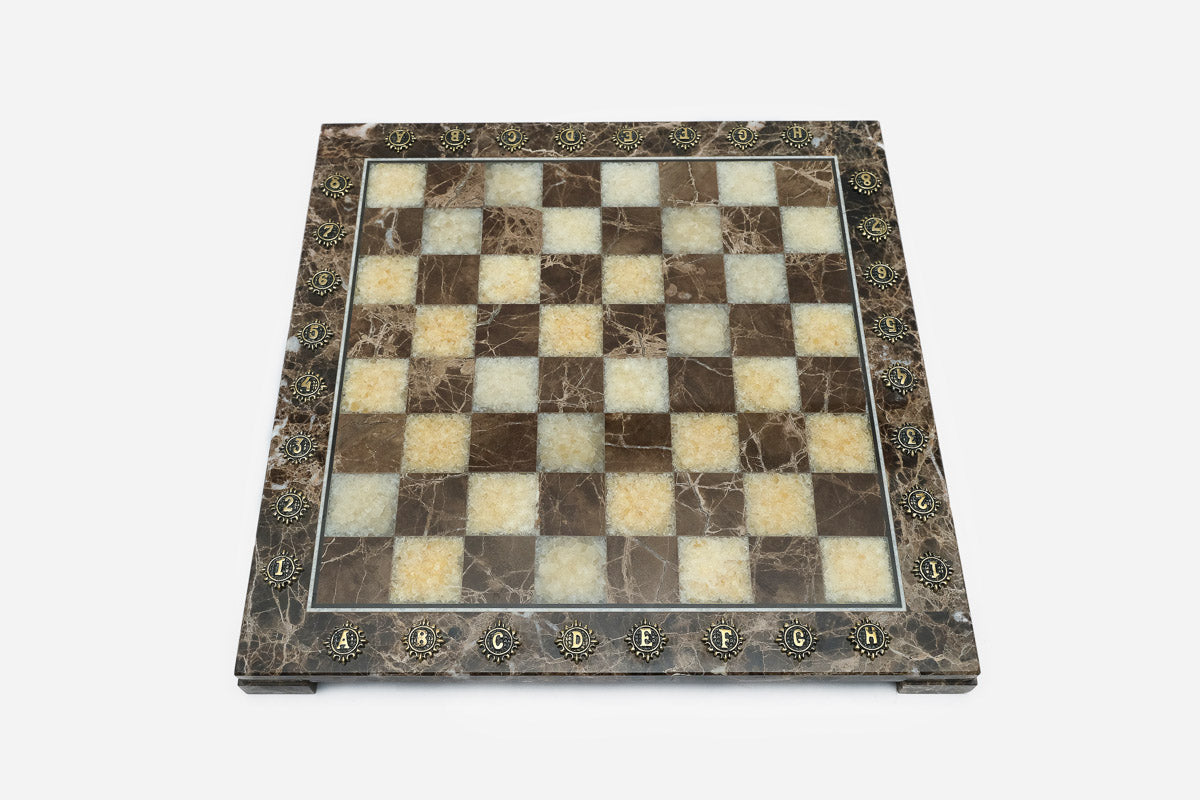 Top-down view of the empty brown and cream marble chess board with brass coordinate medallions
