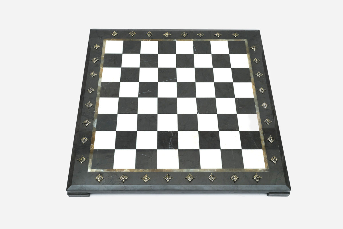 Top-down view of the empty black and white marble chess board with brass coordinate medallions