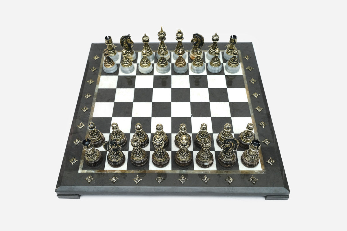 Elevated angle of the black marble chess board with bronze pieces and brass coordinate medallions