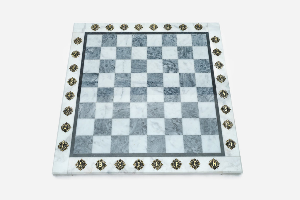 Top-down view of the empty grey and white marble chess board with brass coordinate medallions
