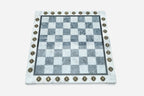 Top-down view of the empty grey and white marble chess board with brass coordinate medallions