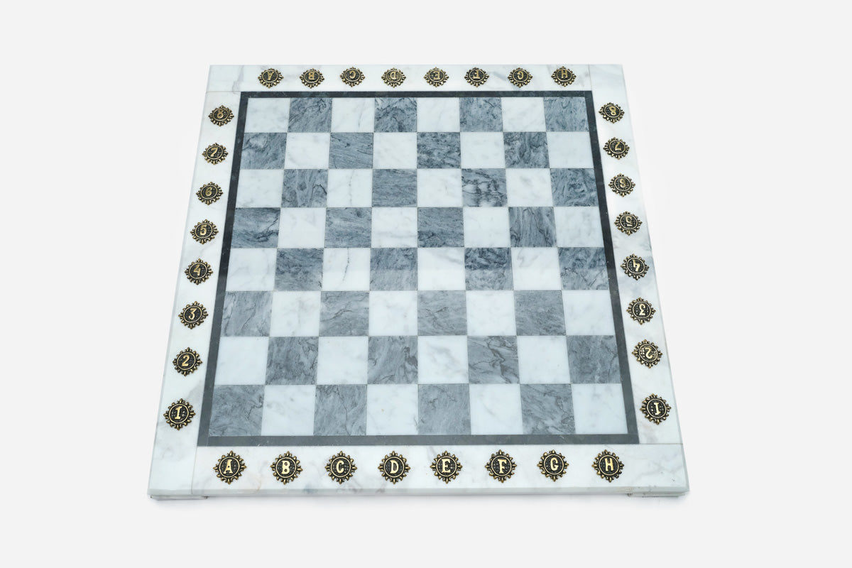 Top-down view of the empty grey and white marble chess board with brass coordinate medallions