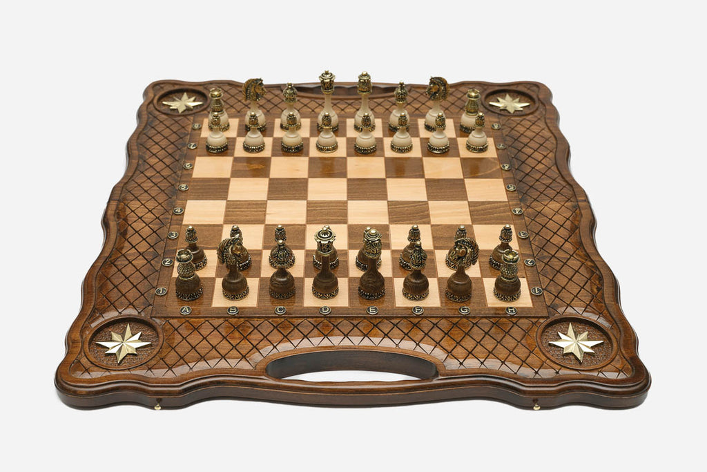 Carved chess board with four brass star inlays, lattice borders and ornate bronze-and-cream figural pieces set up for play