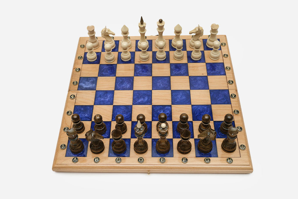 Compact folding chess board in pale wood with royal-blue epoxy squares and wooden pieces set up for play