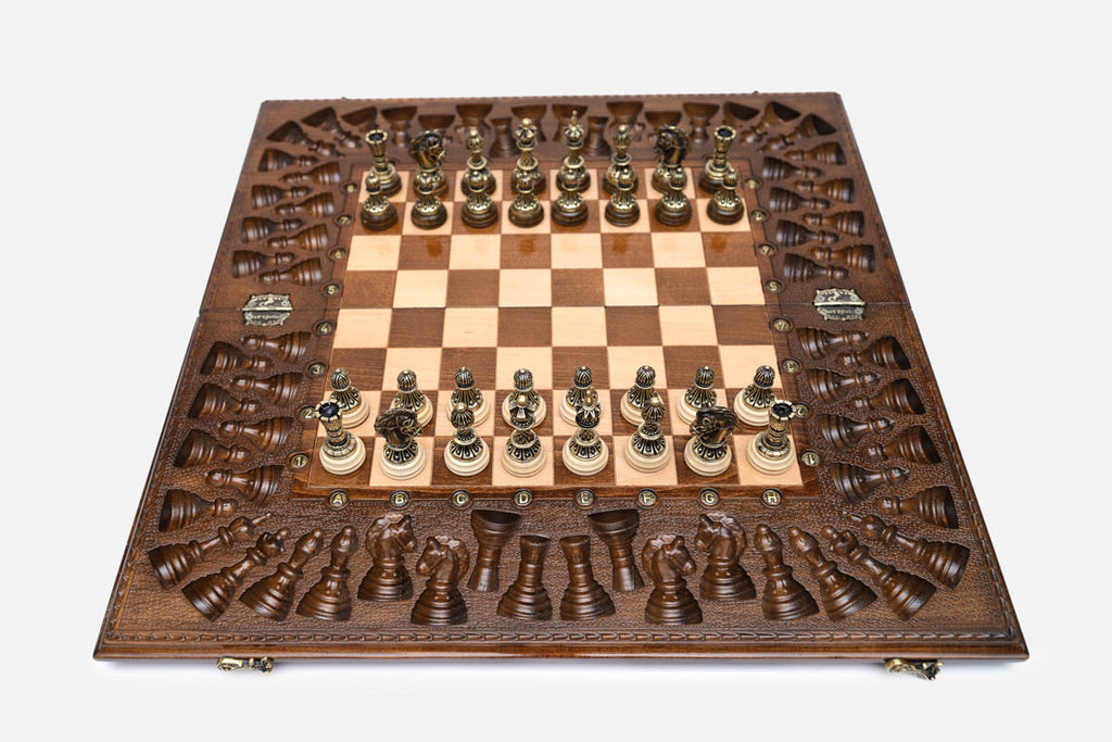 Large opened chess board with ornate bronze-and-wood chess pieces set up, framed by a deeply carved backgammon border