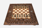 Large opened chess board with ornate bronze-and-wood chess pieces set up, framed by a deeply carved backgammon border
