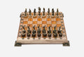 Chess board in pale wood with orange epoxy squares, brass corner brackets and figural bronze Greek-warrior pieces set up for play