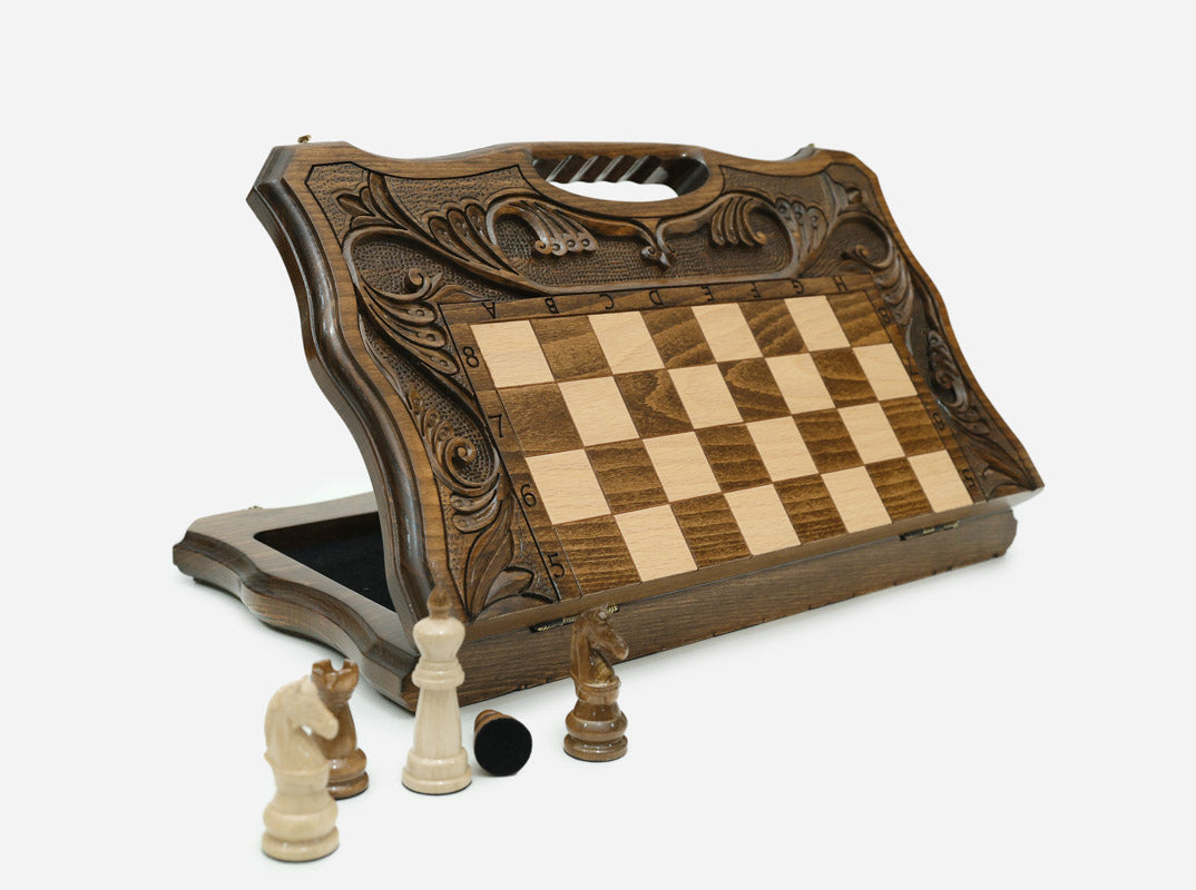 Hand-carved folding chess board standing open, showing the chess face and the carved carry handle at the top, with wooden pieces in front