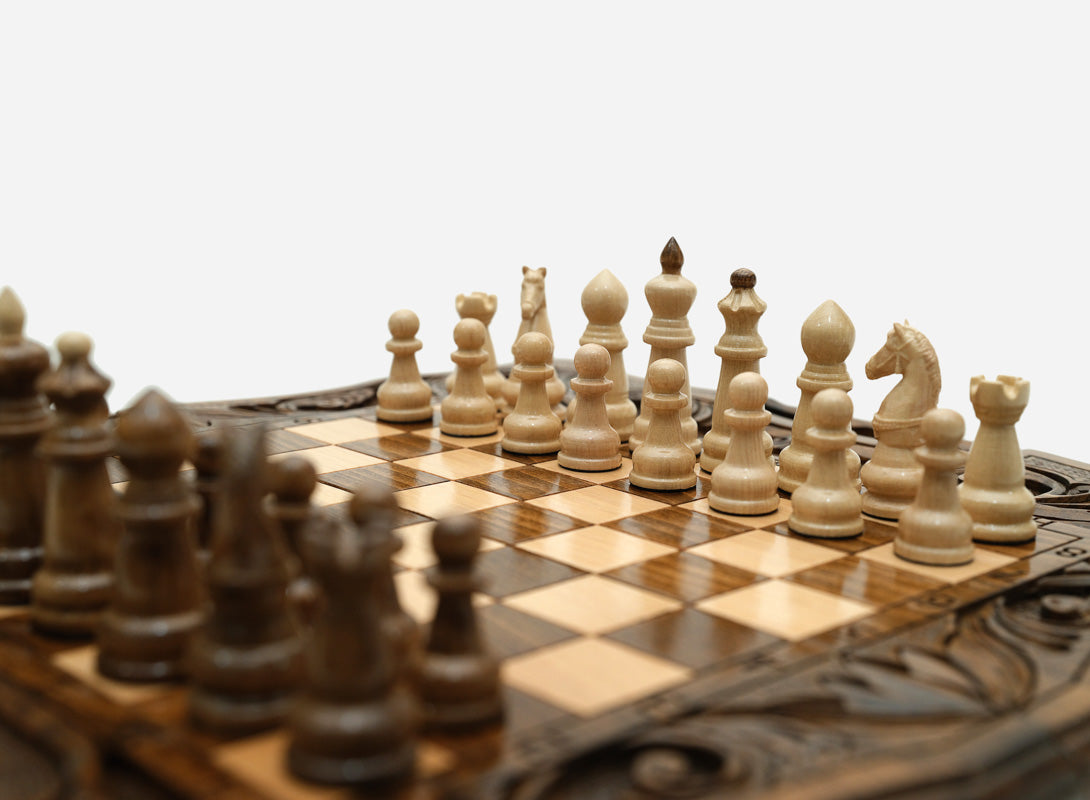 Overhead view of the carved chess board with the full set of light and dark wooden pieces in starting position