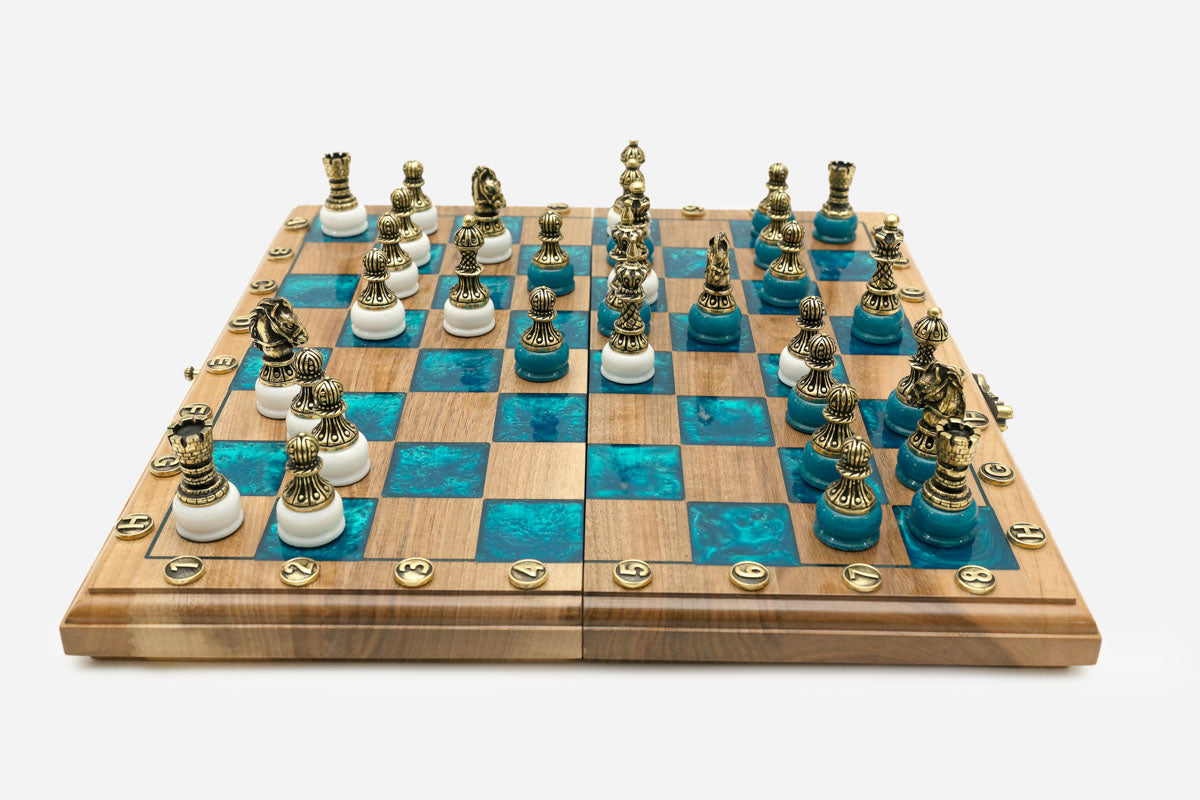 Folding walnut chess board with turquoise epoxy squares and ornate bronze figural pieces on white bases set up for play