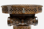 Close-up of the woven Celtic-knot carved apron with a brass pendant, above the fluted column