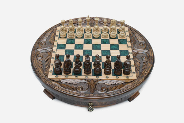 Round carved wooden chess set with emerald-green epoxy resin squares and wooden Staunton pieces arranged for play