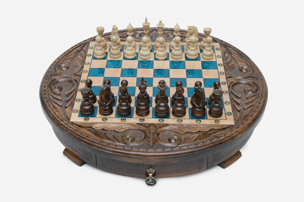 Round carved wooden chess set with turquoise-blue epoxy resin squares and wooden Staunton pieces set up for play