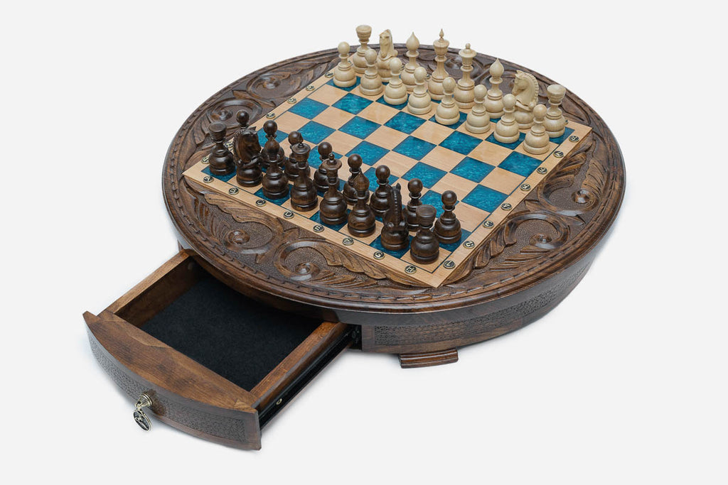 The round chess set with its storage drawer pulled open, revealing black felt lining and a brass pendant pull