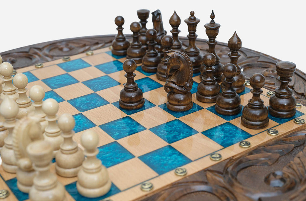 Angled close-up of the dark walnut chess pieces on the blue epoxy board above the open storage drawer