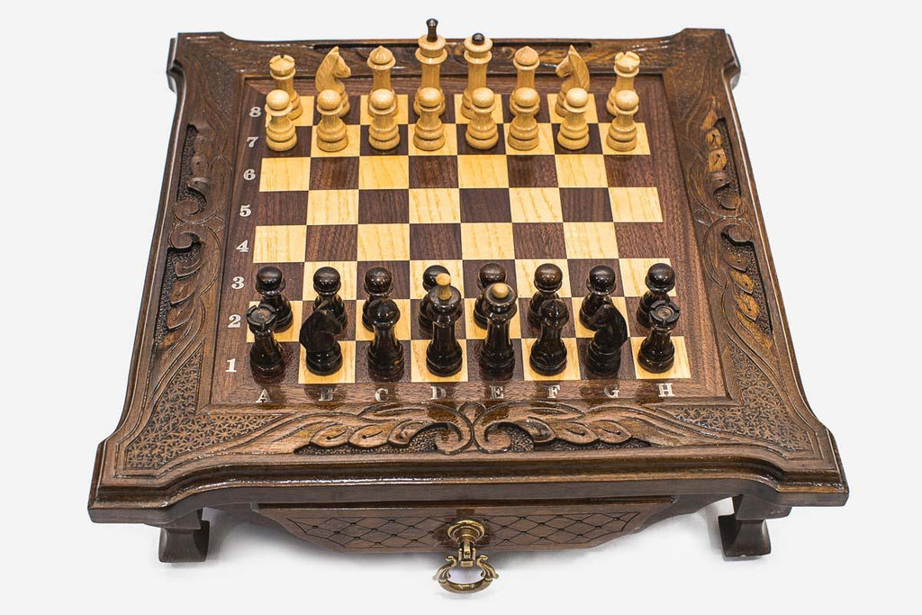 Compact dark walnut chess set with scroll-carved corners and Staunton pieces set up on the inlaid board
