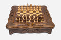 Compact carved wooden chess set with scalloped frame and Staunton pieces set up on the honey-walnut board