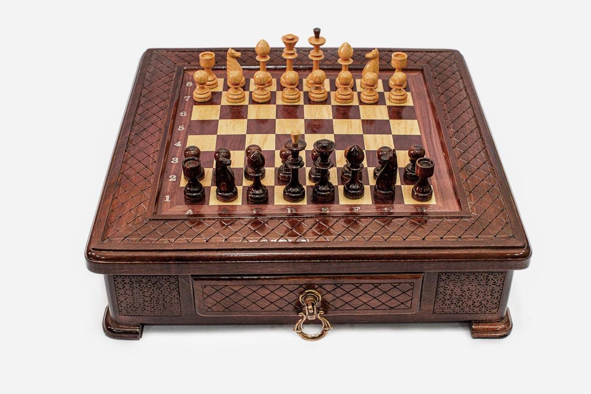 Compact wooden chess set with diamond-lattice carved border and Staunton pieces set up on the inlaid board