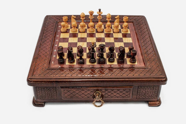 Compact wooden chess set with diamond-lattice carved border and Staunton pieces set up on the inlaid board