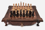 Dark walnut wooden chess set with scroll-carved corners and Staunton pieces set up on the inlaid board