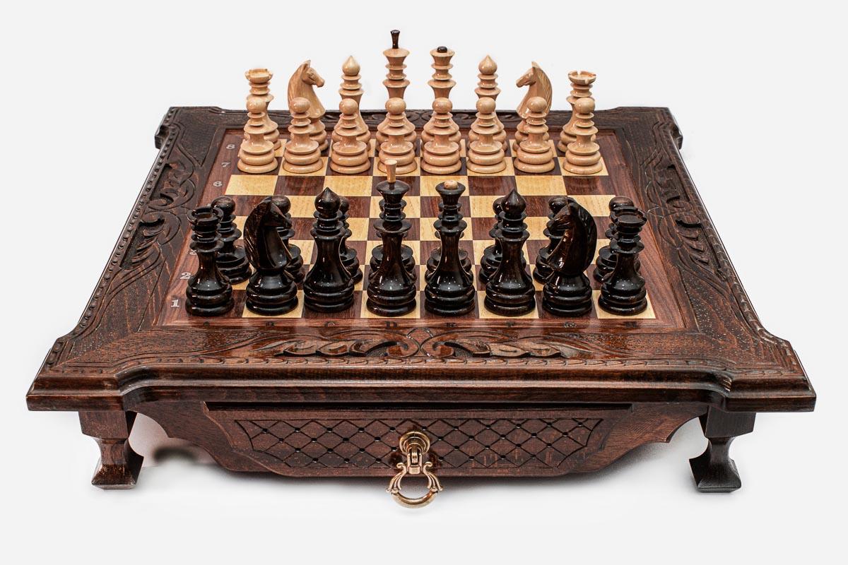 Dark walnut wooden chess set with scroll-carved corners and Staunton pieces set up on the inlaid board