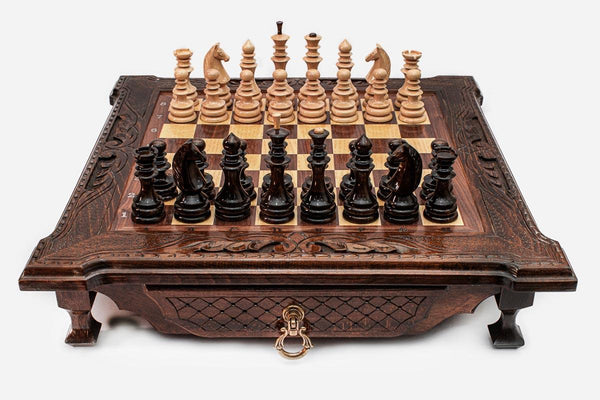 Dark walnut wooden chess set with scroll-carved corners and Staunton pieces set up on the inlaid board