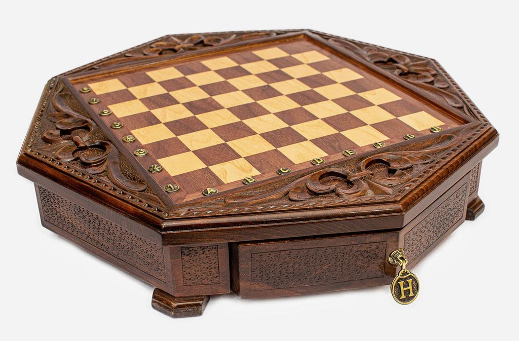 Angled view of the empty octagonal chess board with carved fleur-de-lis border and brass drawer pendant