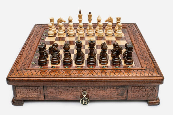 Square wooden chess set with carved diamond-lattice border and Staunton pieces set up on the walnut and maple board