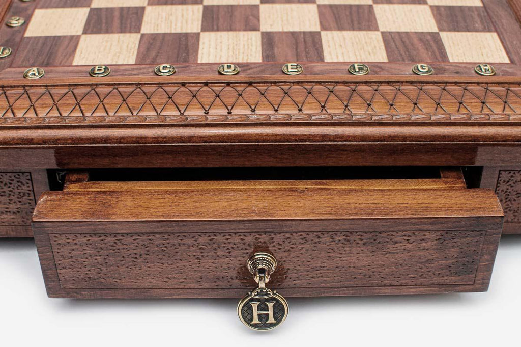 Close-up of the square chess set's carved lattice border and open storage drawer with brass H pendant
