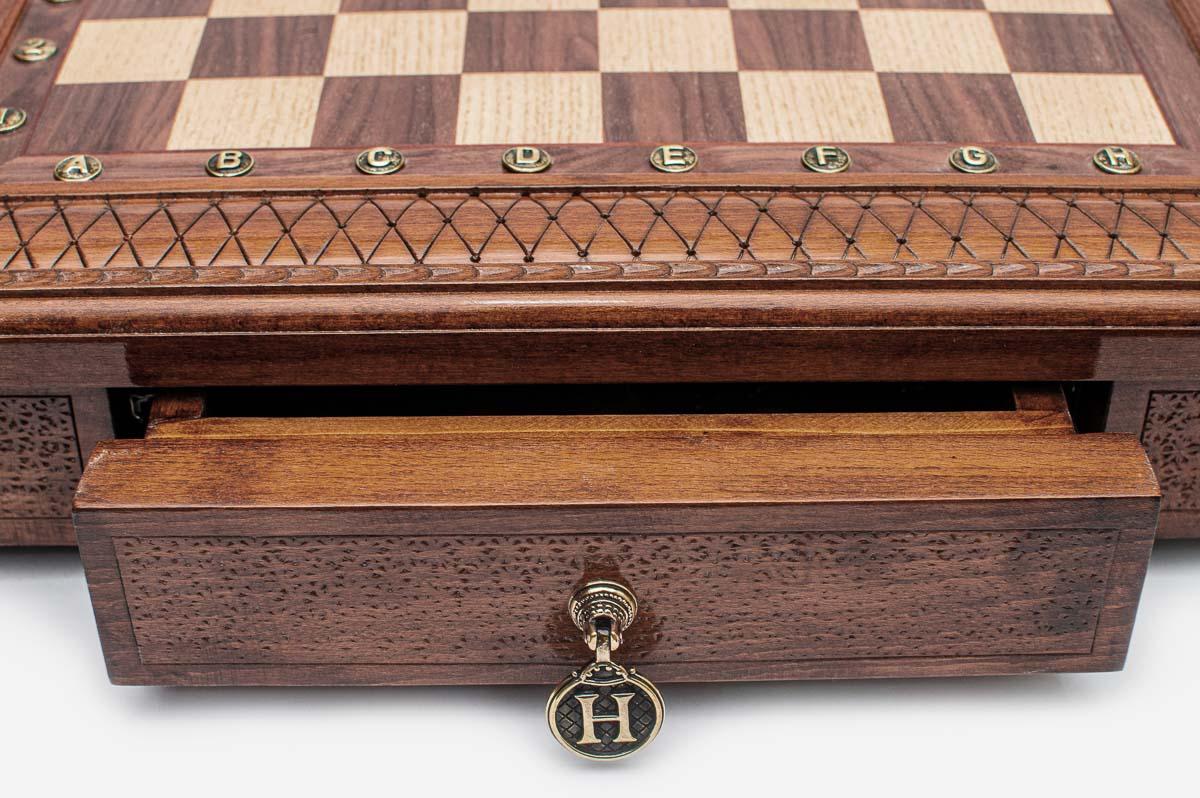 Close-up of the square chess set's carved lattice border and open storage drawer with brass H pendant