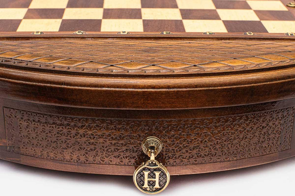 Detail of the round chess set's carved base and brass H drawer pendant