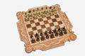 Ornately carved chess board in pale maple with floral corner medallions, ribbon scrollwork and a carved crown, set with bronze-topped wooden pieces