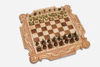 Ornately carved chess board in pale maple with floral corner medallions, ribbon scrollwork and a carved crown, set with bronze-topped wooden pieces