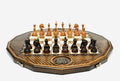 Twelve-sided carved chess board with inlaid coat-of-arms medallions and turned wooden pieces set up for play