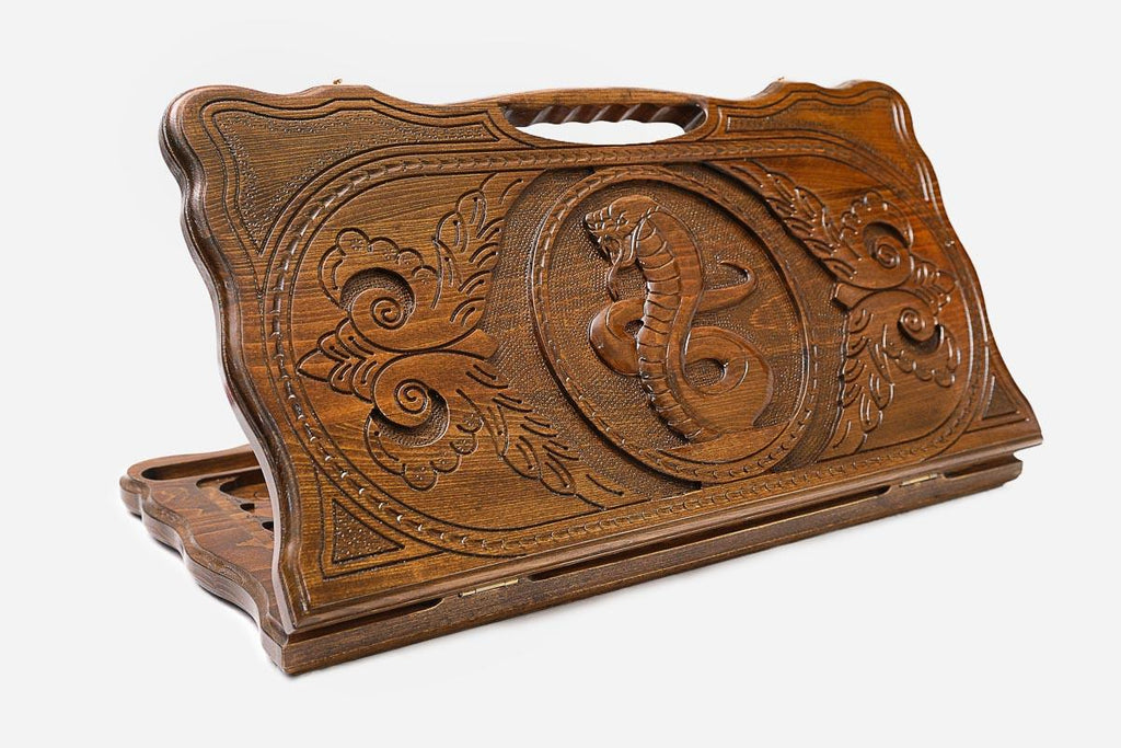 Carved beechwood backgammon board with twin serpents around a floral medallion and a carry handle, propped open