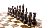 Dark wooden chess pieces on the beech and walnut squares of the travel board