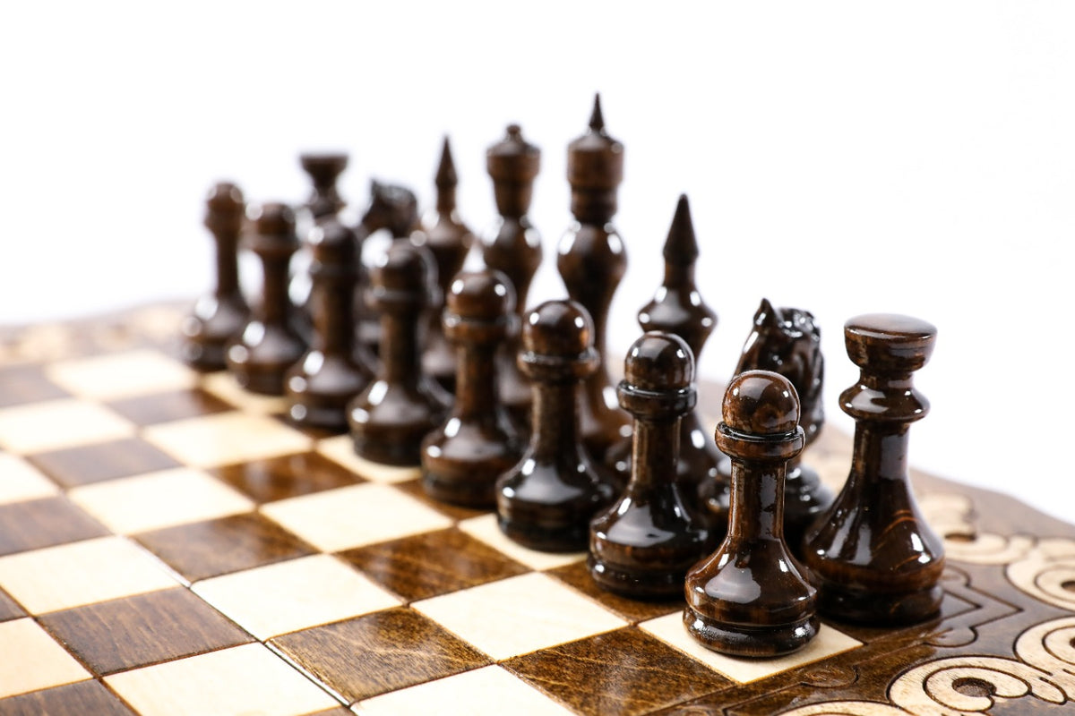 Dark wooden chess pieces on the beech and walnut squares of the travel board