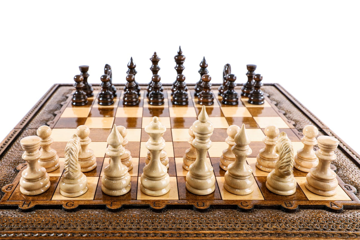 Hand-carved light wood chess pieces in the front rank of the wooden chess board