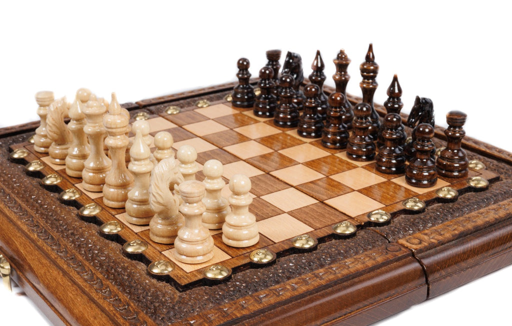 Small handmade chess board with carved textured border and hand-carved wooden pieces, close angle