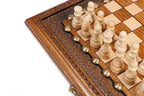 Light hand-carved chess pieces beside the carved frame of the travel chess board