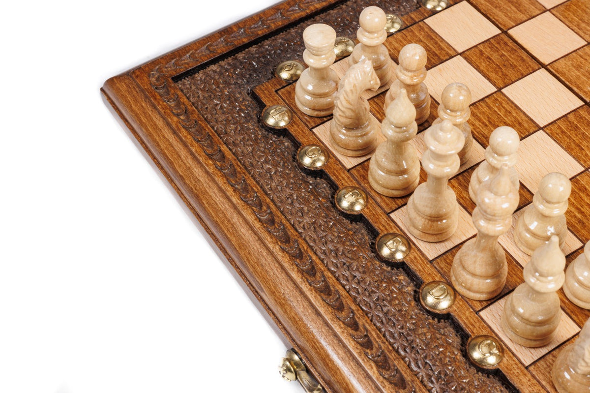 Light hand-carved chess pieces beside the carved frame of the travel chess board
