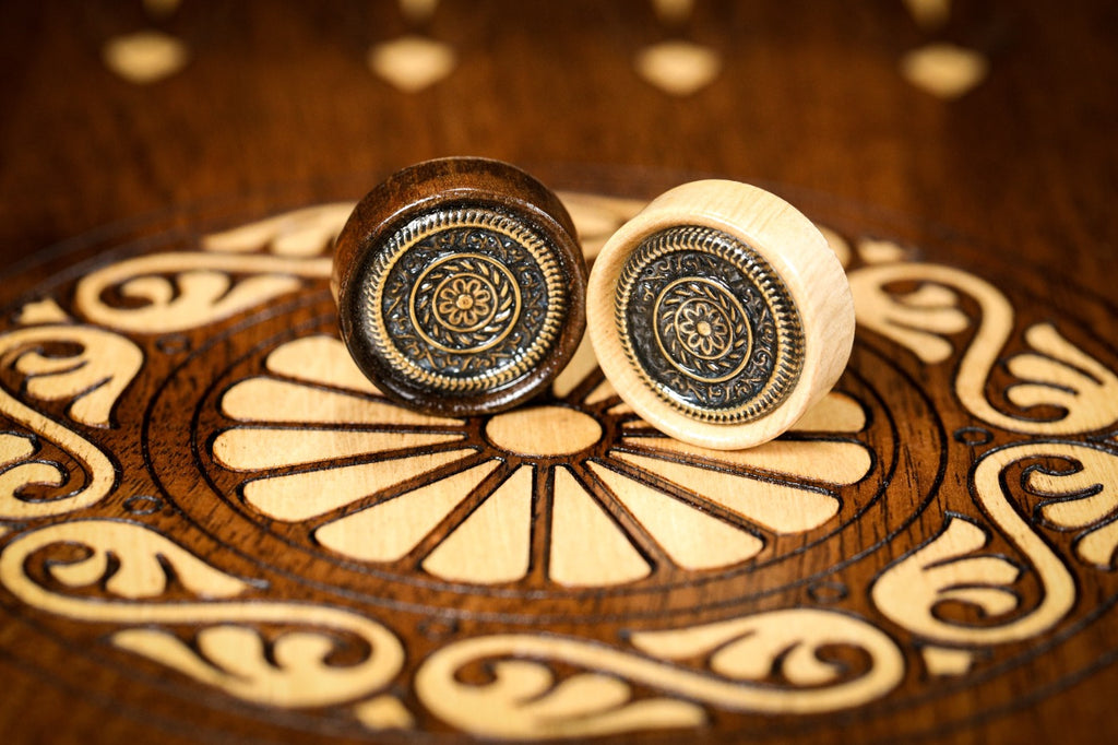 Two ornament checkers with cast emblems, bronze-toned and silver-toned, on the hornbeam wheel inlay