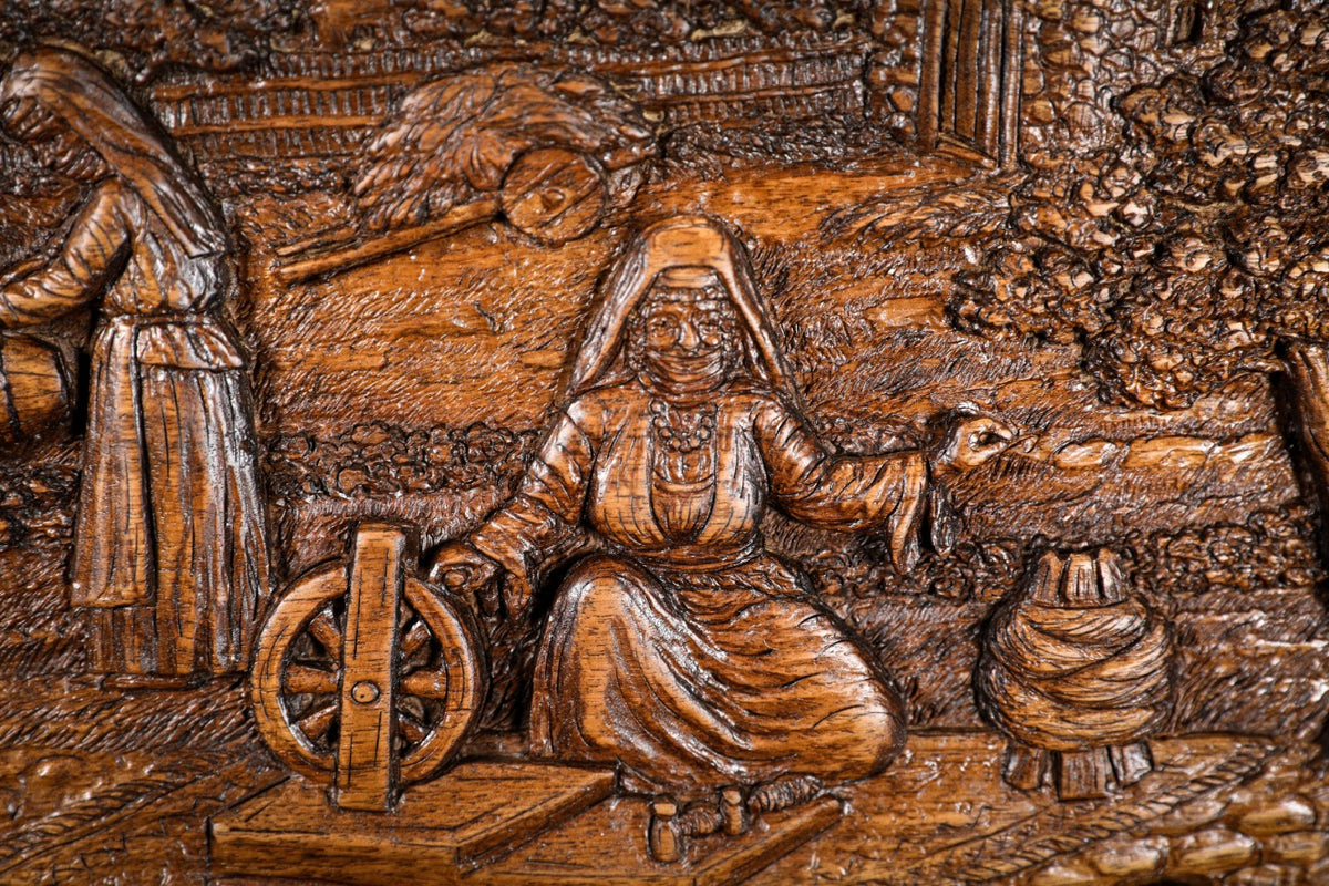 Woman at the spinning wheel with the churn beside her, carved in deep relief, close-up