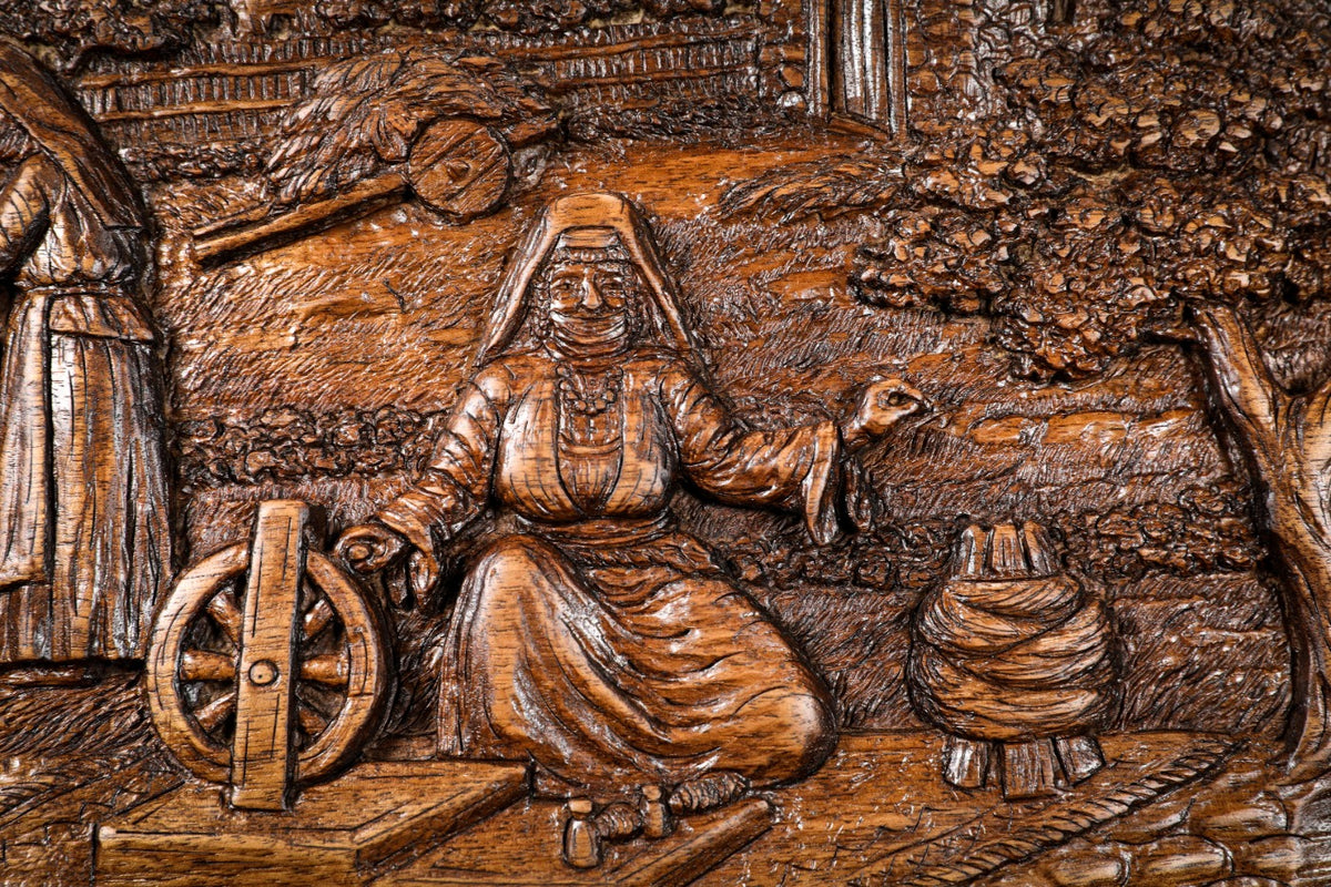 Woman seated at the spinning wheel with the churn behind her, carved in deep relief